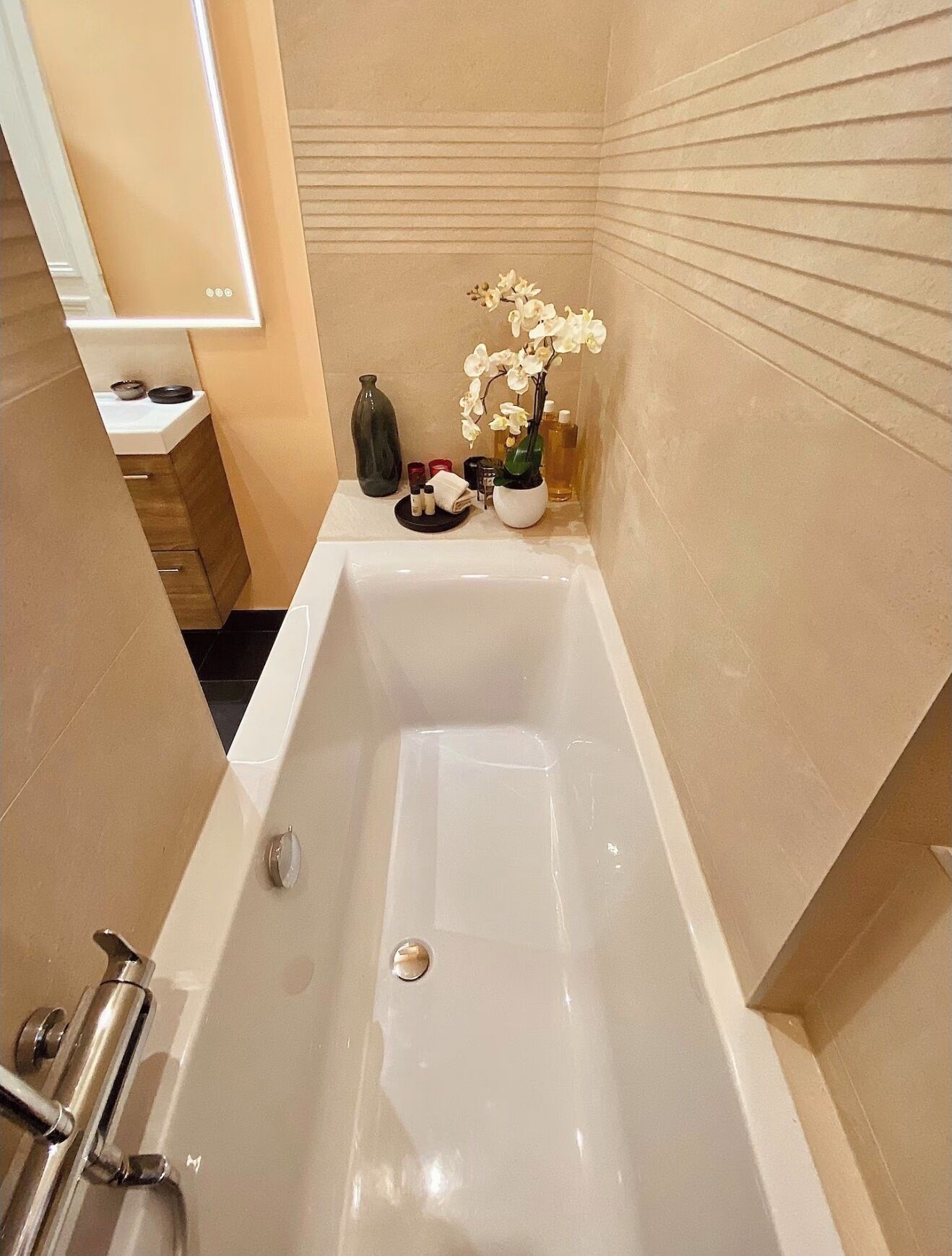 Ein modernes Badezimmer mit einer freistehenden Badewanne, einem kleinen Waschtisch mit Spiegel und einer Zimmerpflanze, einer Orchidee.