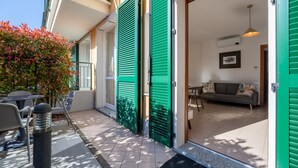 Ein Wohngebäude mit grünen Fensterläden, einem Balkon mit Gartenmöbeln und einem Wohnzimmer mit Sofa und Pendelleuchte.