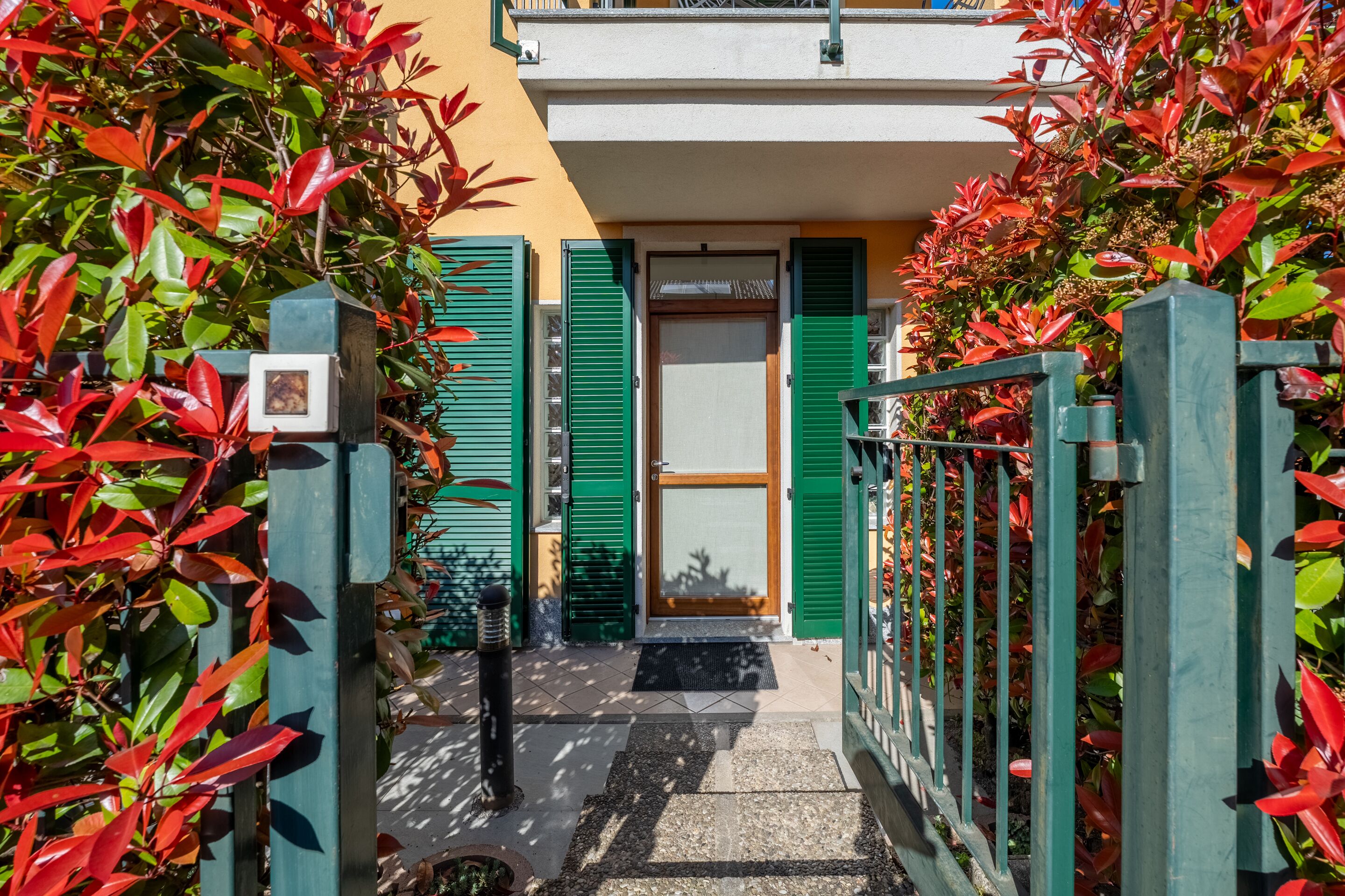 Ein schmaler Weg führt zu einem Gebäude mit grünen Fensterläden und einer Tür.