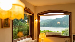 Ein Zimmer mit einer Couch, zwei Lampen und einem großen Bogenfenster mit Blick auf einen See und Berge.