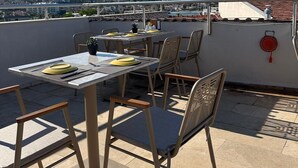 Terraza al aire libre con mesas y sillas, vista de la ciudad y un objeto decorativo rojo en la pared.