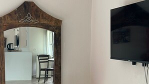 Una habitación con un tocador de madera, un espejo, un televisor montado en la pared y un radiador.