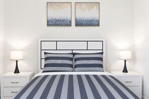 A bedroom with a bed, two bedside tables, two lamps, and two wall-mounted paintings. - Elegant New-Build Suite • Walk to Everything (Hot Springs)