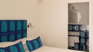 A bedroom with a large bed, a headboard with a geometric pattern, and a bathroom visible through an open door. - Room-terrazza del Sole - Camera Maestral (Positano)