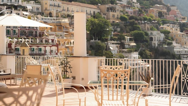 A terrace with wicker chairs and a table, overlooking a hillside of colorful buildings. - Room-terrazza del Sole - Camera Maestral (Positano)
