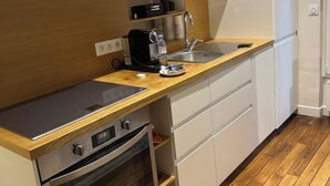Een kleine keuken met een magnetron, koffiezetapparaat, spoelbak en een inbouwoven.