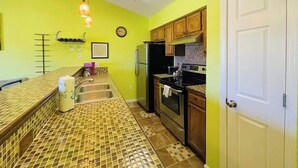 Cozinha com painel de azulejos, eletrodomésticos de aço inoxidável, armários de madeira e uma porta branca.