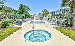 A swimming pool with lounge chairs and umbrellas, surrounded by greenery and a building in the background. - Sunny River Oaks Retreat  2BR Golf Condo (Myrtle Beach)