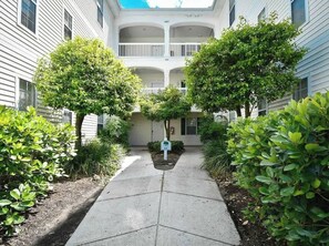 A courtyard with a central pathway flanked by trees and shrubs, leading to a building with a balcony. - Sunny River Oaks Retreat  2BR Golf Condo (Myrtle Beach)
