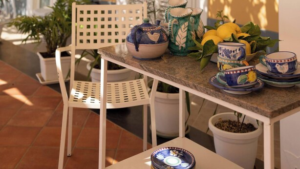 A patio with a table set for dining, surrounded by potted plants and a yellow wall. - Room-terrazza del Sole -camera Levante (Positano)