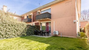 Ein zweistöckiges Gebäude mit einem Balkon, einer Terrasse mit Gartenmöbeln und einem gepflegten Rasen.