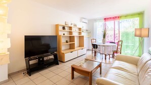 Ein Wohnzimmer mit Fernseher, Holzregalen, einer Couch und einem Esstisch mit Stühlen.