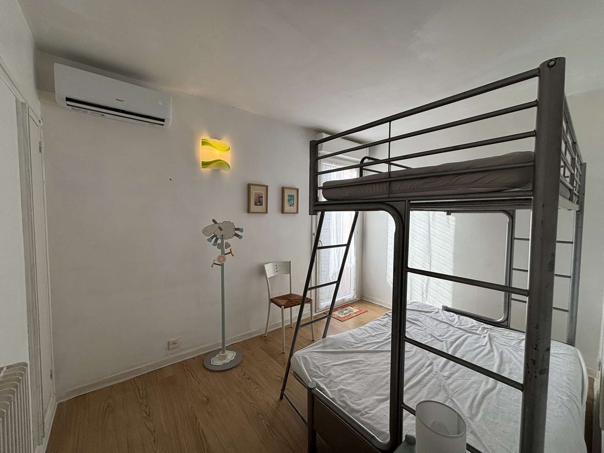Een slaapkamer met stapelbed, een staande lamp, een ingelijst beeld en een airconditioning.