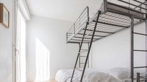 Ein Schlafraum mit Etagenbetten, einer Leiter, einem Fenster und einer Tür.
