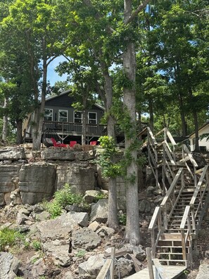 A rustic wooden staircase leading to a house surrounded by large trees and rocky terrain. - Escape to the enchanting Moonrise Bluff Lake House located in Warsaw on LOTO (Warsaw)