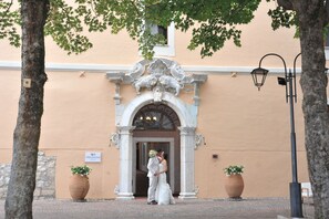 A building entrance with a decorative archway, a sign reading 'Villa Grandi,' and two large potted plants.