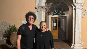 Twee personen staan voor een gebouw met een gebogen entree en een bord waarop 'Villa Grandi' staat.