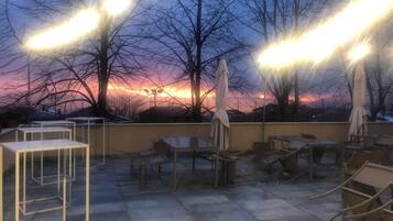 Un espace extérieur aménagé avec des tables, des chaises, des parasols et une vue imprenable sur le coucher de soleil.