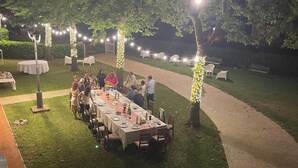 Een buiten eethoek met tafels en stoelen, lichtjes en bomen.