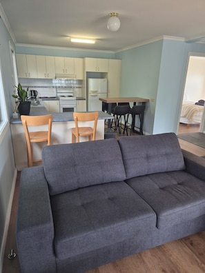 Una sala de estar moderna con un sofá gris, sillas de madera, una mesa de comedor y una cocina al fondo.