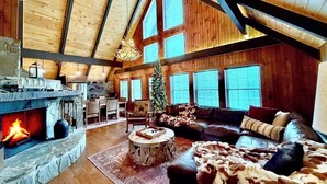 Amplia sala de estar con chimenea de piedra, sofá de cuero y un árbol de Navidad.