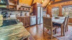 Una cocina rústica con vigas de madera, encimera de mármol y comedor con mesa y sillas.