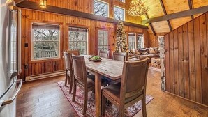 Un comedor amplio con una mesa y sillas de madera, ventanas grandes y una araña.
