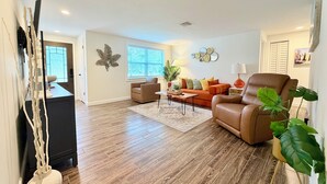 A living room with a brown leather sofa, a coffee table, and a large window. - Salt water beach/City vibe vacation home. (Largo)