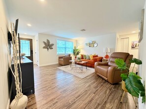 A living room with a brown leather sofa, a coffee table, and a large window. - Salt water beach/City vibe vacation home. (Largo)