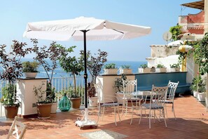 A terrace with white metal chairs and a table, surrounded by potted plants and a white umbrella. - Villa Esclusiva con Vista Panoramica su Positano (Positano)