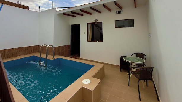 Une piscine avec un escalier métallique, une petite table avec des chaises et une porte donnant sur un escalier.