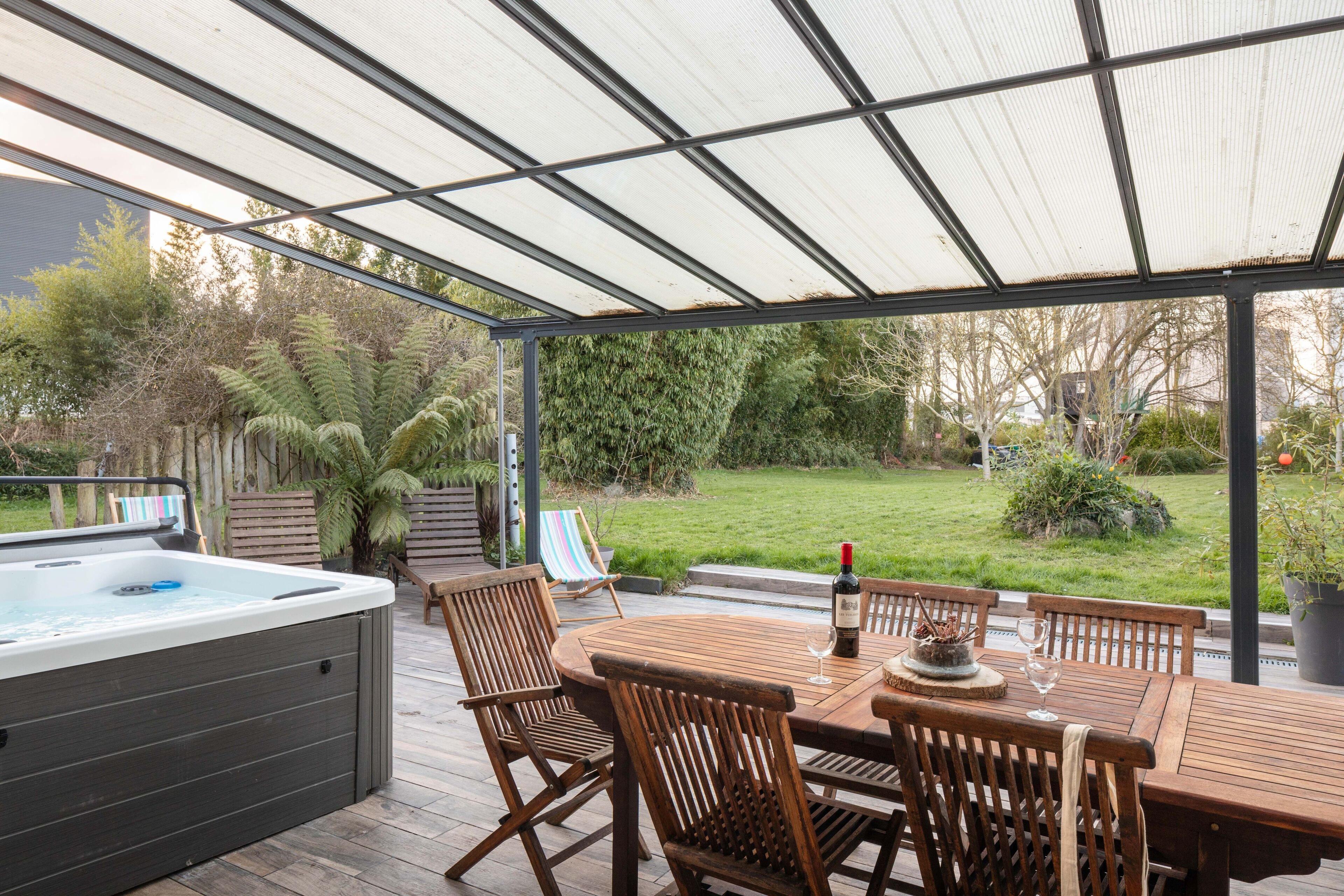 Un patio couvert avec un jacuzzi, une table en bois et des chaises.
