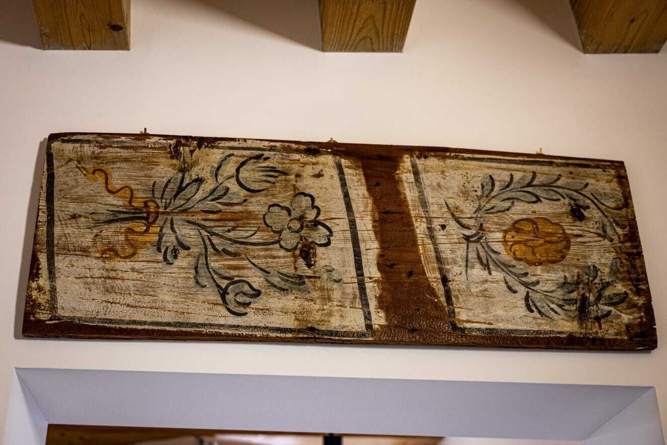 A rustic wooden panel with floral designs, mounted on a plain wall.