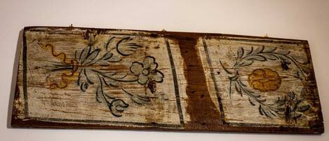 A rustic wooden panel with floral designs, mounted on a plain wall.