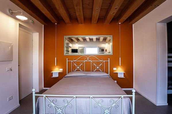 A bedroom with a bed, wooden ceiling beams, a mirror above the bed, and wall-mounted lights. - Panormos 91 Rooms & Terrace (Palermo)