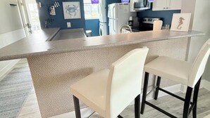 Uma cozinha moderna com ilha central, luminárias pendentes e um aviso que diz "LIFE'S BETTER AT THE BEACH".