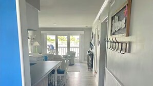 Cozinha moderna com bancada branca, área de refeições com cadeiras e corredor com tapete estampado.