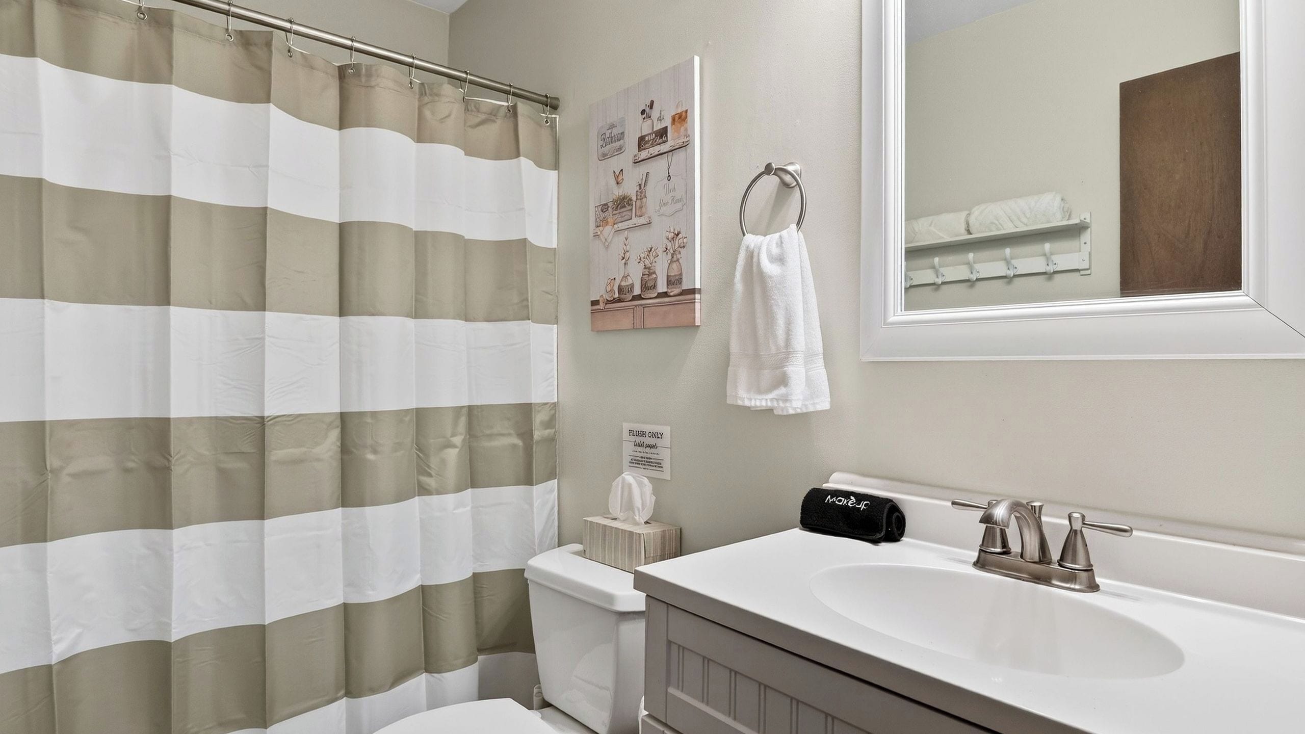 Une salle de bain avec un rideau de douche à rayures, un lavabo, un miroir et un porte-serviettes.