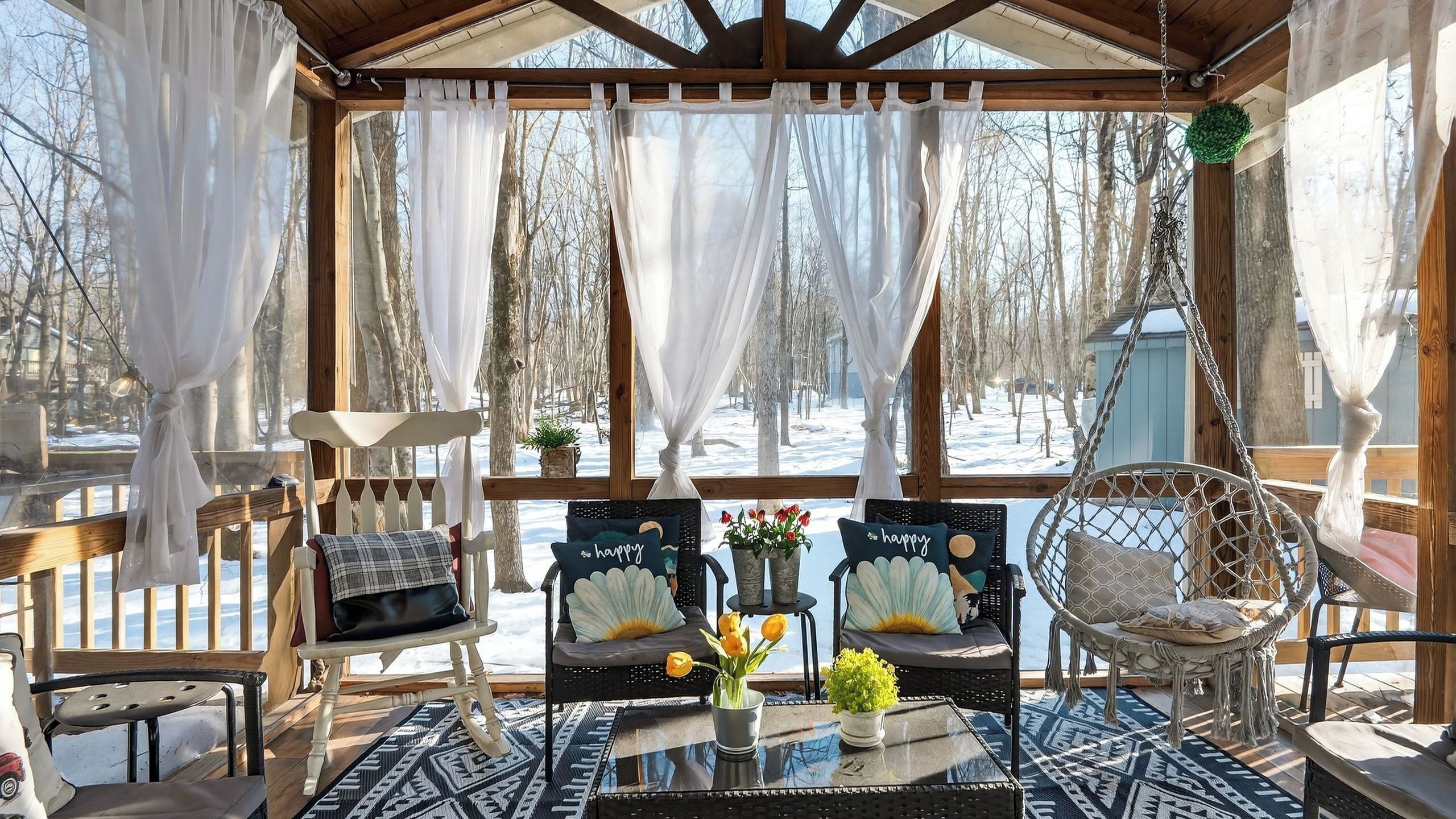 Een gezellig buitenverblijf met een houten pergola, comfortabele stoelen, een hangstoel en uitzicht op een besneeerd landschap.