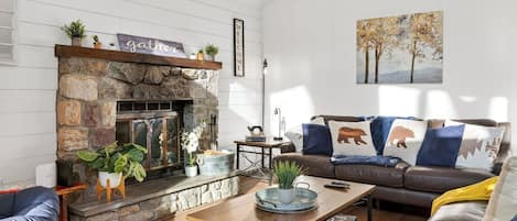 Una sala de estar acogedora con chimenea de piedra, un sofá con cojines estampados y un cuadro en la pared.