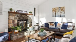 A cozy living room with a stone fireplace, a sofa with patterned cushions, and a painting on the wall. - Emberwood Cabin by Avantstay Poconos Cabin + Firepit + Private Deck + Outdoor Dining + Near Jack Frost Skiing (Albrightsville)