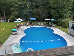 Un jardin avec une piscine, des chaises longues, des parasols et un petit abri de jardin.