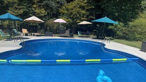 Piscina com um flutuador azul, rodeada por espreguiçadeiras e guarda-sóis.