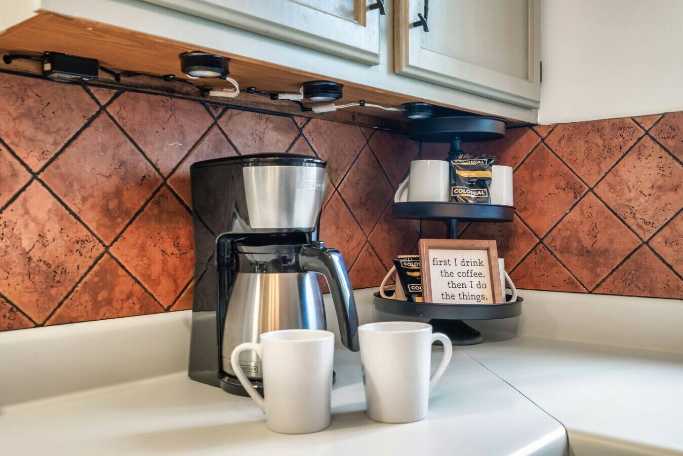 Une cuisine équipée d’une machine à café, de deux tasses blanches et d’un plateau contenant des capsules de café.