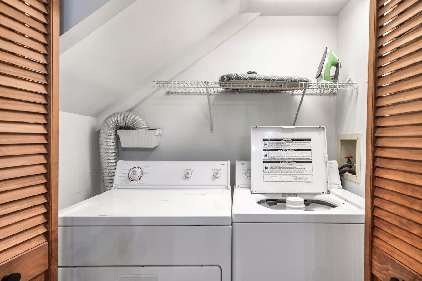 A compact laundry area with a washing machine, dryer, and a shelf with an iron and other items.