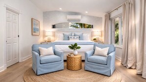 Un dormitorio con una cama grande, dos sillones, un tapete redondo tejido y una mesita de noche con una planta.