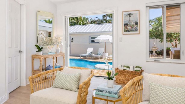 Habitación con muebles de mimbre, vista a una piscina y puerta que da a un área exterior con sillas de descanso.