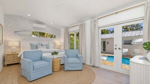 Un dormitorio con cama, dos sillones, alfombra redonda y vistas a una piscina exterior.