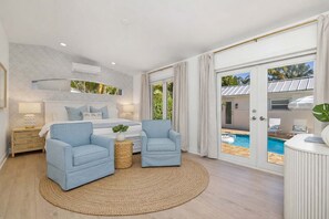 Ein Schlafzimmer mit einem Bett, zwei Sesseln, einem runden Teppich und Blick auf einen Außenpool.