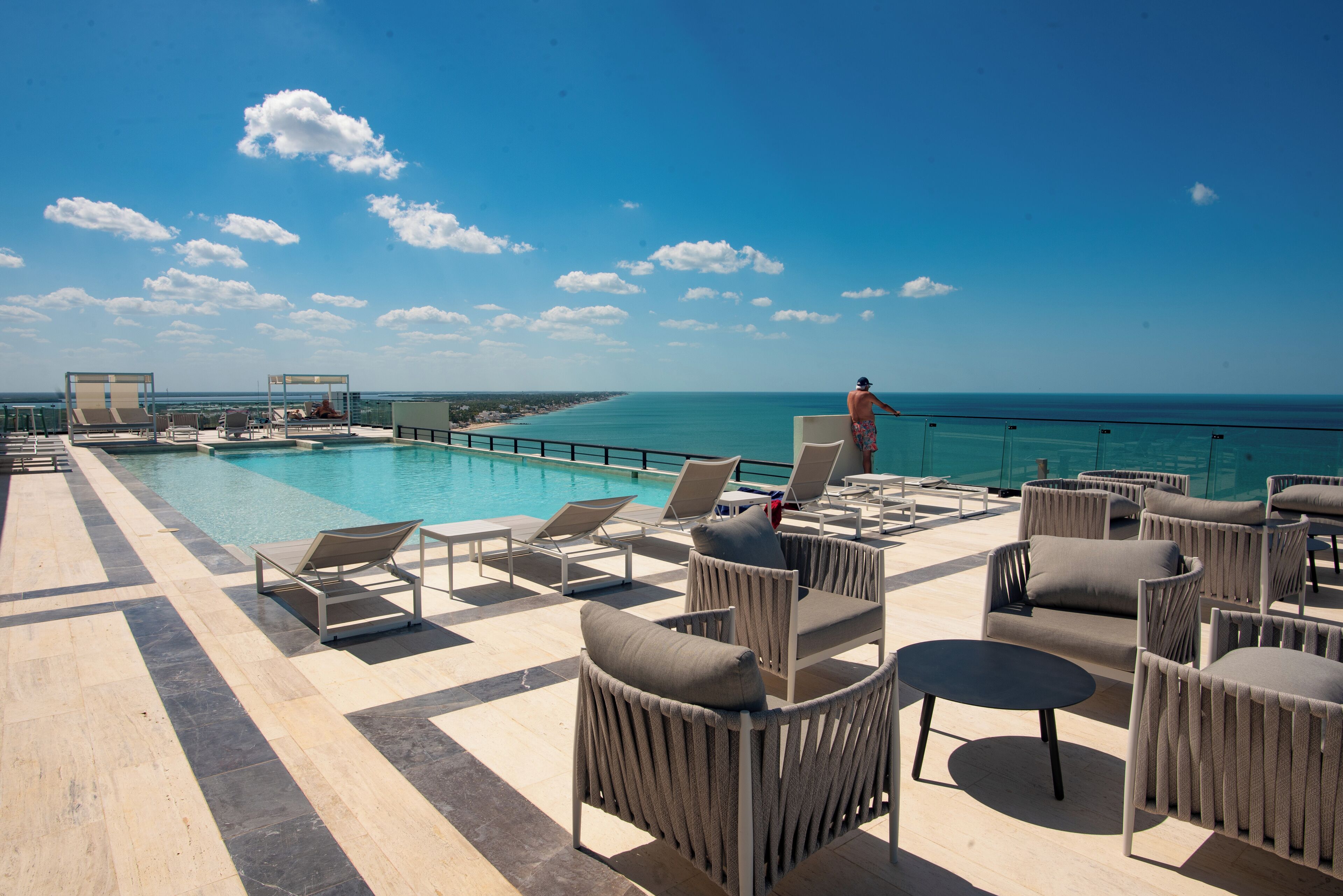 Un espace piscine aménagé sur le toit, avec des chaises longues et une vue sur l’océan.